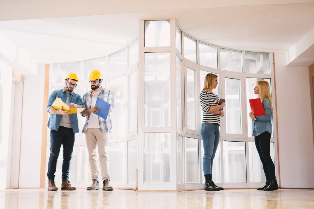 two focused young professional engineers with helmets looking project papers while another side female designers consulting about ideas